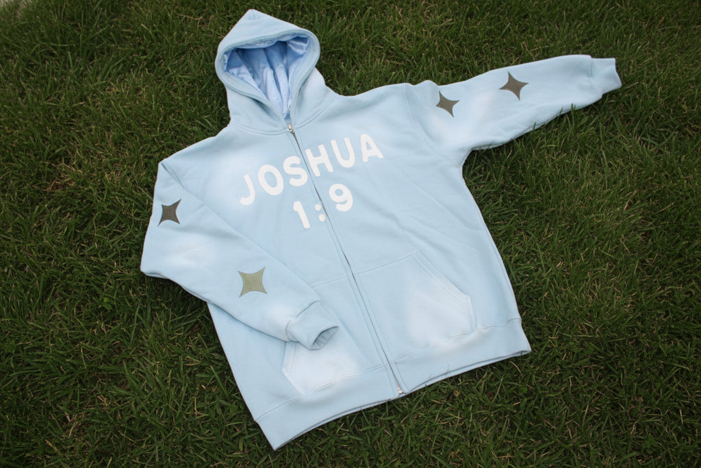 Light blue jacket  with embroidered 'JOSHUA 1:9' text outside on the grass